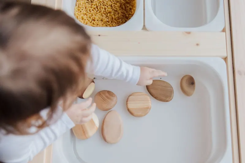 Un enfant manipule des disques en bois dans un plateau
