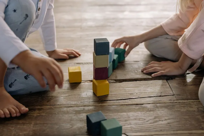 Deux enfants empilent des cubes en bois sur un parquet